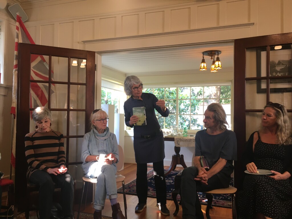 Photo of Katherine Lawrence reading from Black Umbrella at Joy Kogawa House with four other attendees sitting and listening