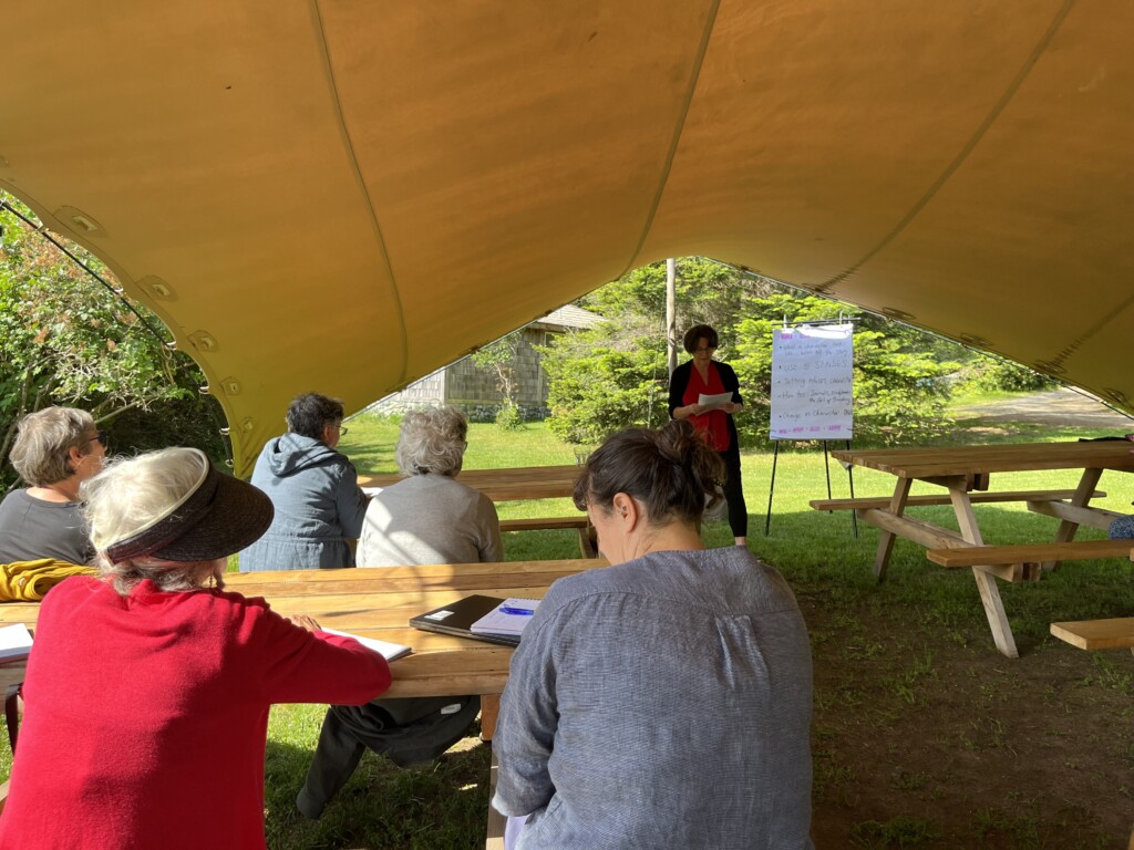 Shaena Lambert teaching various attendees outside under a tent on a sunny at 2023's Tapping the Stream, Hollyhock, Cortes Island, BC
